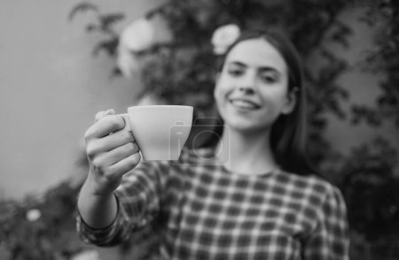 Téléchargez les photos : Modèle féminin tenant une tasse de café. Une femme qui donne du café. Portrait de jolie jeune femme dans le parc avec tasse de café pendant la journée de printemps - en image libre de droit