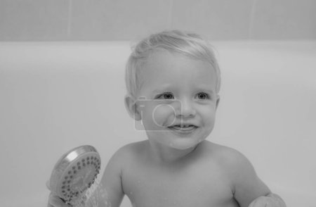 Foto de Divertido lindo bebé está nadando en espuma en el baño. Lindo niño tomando baño jugando con espuma y juguetes de pato en un baño blanco y soleado - Imagen libre de derechos