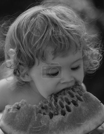Téléchargez les photos : Joyeux enfant mangeant pastèque. Enfant bébé mangeant pastèque dans le jardin, gros plan sur le visage. Les enfants mangent des fruits dehors. Enfant jouant dans le jardin mordant une tranche de pastèque - en image libre de droit