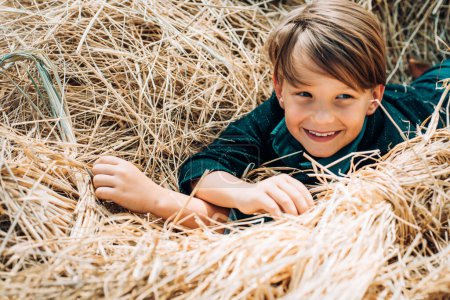 Foto de Lindo niño pequeño sosteniendo la hoja de oro en el fondo de la aldea granja. Niño yace en el heno - Imagen libre de derechos