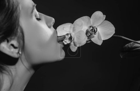 Foto de Sexy chica lamer flor de orquídea. Orquídeas lengua oral. Sensual joven mujer chupar orquídea floral. Liras rojas con lápiz labial - Imagen libre de derechos