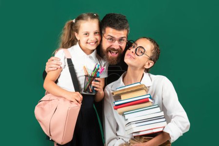 Photo for Portrait of father and school kids daughters hugging on blackboard background. Reading book and writing. Dad teaching schoolchild girls in classroom - Royalty Free Image