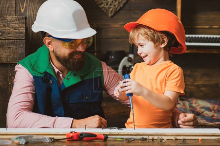 Photo for Little son helping his father with building work. Parent in protective helmet teaching little son to use different tools in school workshop - Royalty Free Image