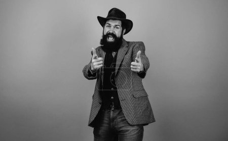 Photo for Handsome bearded hipster man in blazer and hat isolated at orange background. Gentleman in plaided jacket showing his fingers at camera. Happy emotional bearded man - Royalty Free Image