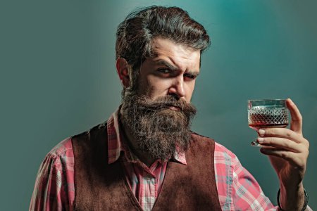 Téléchargez les photos : Hipster avec barbe et moustache en costume boit de l'alcool après la journée de travail. Homme ou homme d'affaires boit du whisky sur fond noir - en image libre de droit