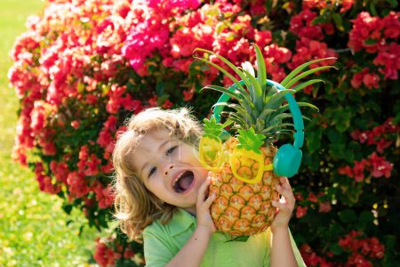 Téléchargez les photos : Enfant garçon tenant l'ananas souriant avec un visage heureux. Fruits d'été - en image libre de droit
