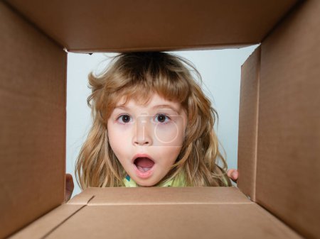 Photo for Surprised child boy unpacking, opening carton box and looking inside. The package, delivery, surprise, gift for kid. Children emotions and kids facial expressions concepts. Parcels and delivery - Royalty Free Image