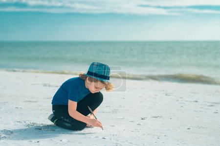 Téléchargez les photos : Face d'enfant d'été. Enfant mignon dessiner un sur le sable profiter de la mer d'été et de rêver. Un visage d'enfant rêveur. Portrait d'enfant rêveur de jour de près. Rêves et imagination - en image libre de droit