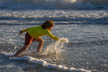 Photo for Happy child playing in splashing water on summer sea. Summer vacation. Kid play of waves at sea. little kid playing in sea and splashes water drops. Child play splash water on sea. Summer vacation - Royalty Free Image