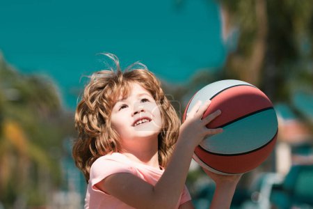Foto de Lindo chico sonriente juega baloncesto. Niños activos disfrutando de juego al aire libre con pelota cesta - Imagen libre de derechos