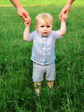 Photo for Baby child on the green grass in summer park. Parents hand and child. Perfect family holding hands, adopted child being supported by loving parents - Royalty Free Image