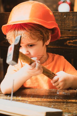 Foto de Lindo niño en sombrero duro sosteniendo tablón de madera y martillo. - Imagen libre de derechos