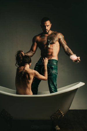 Foto de Brutal barbudo hombre tatuado con mujer desnuda sexy acostado en el baño. Hombre musculoso guapo sostiene champagne refrigerador y botella. Hermosa chica abre los hombres vuelan antes del sexo. Un par de preliminares - Imagen libre de derechos