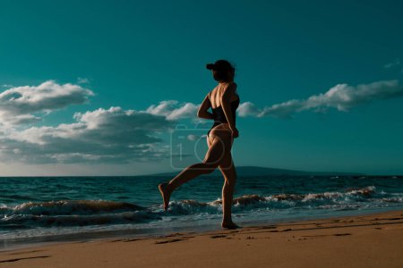 Téléchargez les photos : Silhouette d'une jeune femme courant le long de la plage de la mer - en image libre de droit