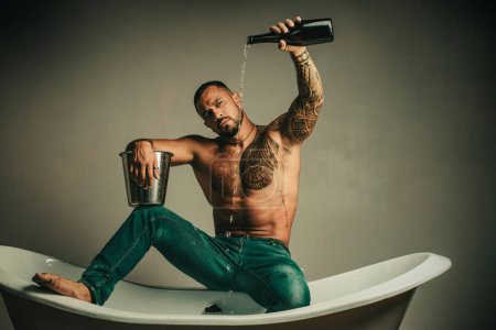 Téléchargez les photos : Homme déshabillé sexy assis sur la baignoire dans la salle de bain, les hommes vacances avec du champagne. Célébrer Noël ou anniversaire. Partie de sexe privé - en image libre de droit