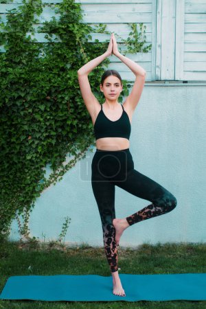 Foto de Yogi woman practicing yoga, vrksasana exercise. Young beautiful woman in sports outfits doing stretching before workout outdoor. Fit girl in sportswear doing morning yoga - Imagen libre de derechos