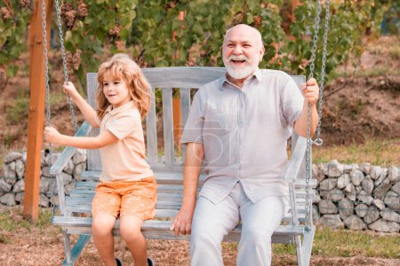 Foto de Grandfather and son swinging in garden. Granddad and grandchild playing on swing - Imagen libre de derechos