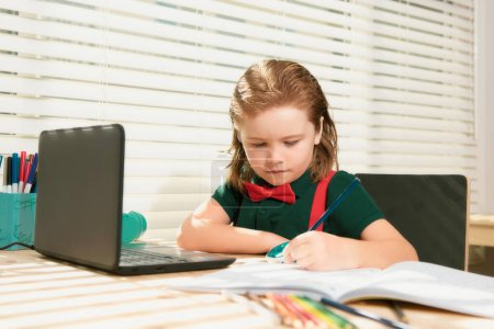 Photo for Smart school boy does homework in school class. Writes text from laptop notebook - Royalty Free Image