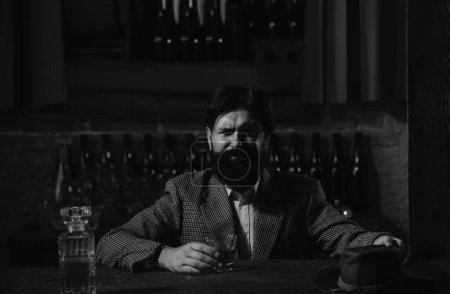 Foto de El hombre con barba sostiene brandy de vidrio, bebe coñac en el pub. El tipo hipster sabe a bebida. Bebiendo whisky. Vida nocturna de lujo, hombre barbudo rico beber bebidas caras - Imagen libre de derechos