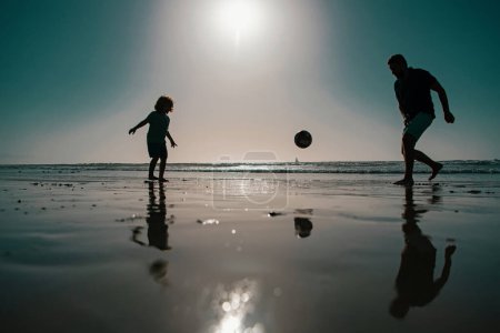Photo for Daddy with kid boy playing on a summer day. Father and son play soccer or football on the beach on summer family holidays - Royalty Free Image