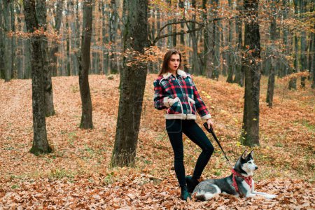 Photo for Woman with her dog chose a great place to stroll because the paints of autumn forest makes some mood feeling. Autumn walk and petting concept - Royalty Free Image