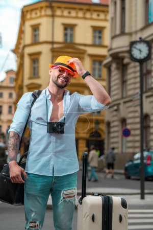 Foto de Hombre turista viajero en ropa casual sombrero con maleta. Hombre de negocios en viaje de negocios caminando con bolsa de viaje en la calle de la ciudad. Viajante hombre de negocios - Imagen libre de derechos