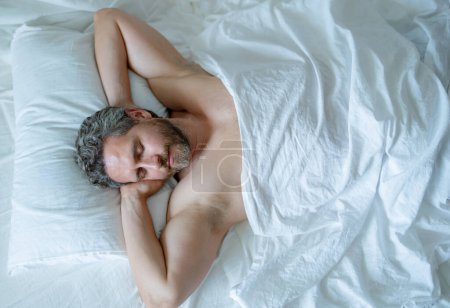 Photo for Man sleeping in bed. Top view of handsome man sleeping in bed. Morning healthy sleep. Guy sleeping on bed in bedroom. Middle aged adult man is sleeping at home. Cozy bed, white pillow mattress - Royalty Free Image