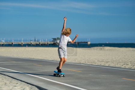 Foto de Feliz niño activo aprendiendo a equilibrarse en el skateboard jugando en la calle. Cabalgando y se ve feliz. Niño jugando surf skate o monopatín al aire libre - Imagen libre de derechos