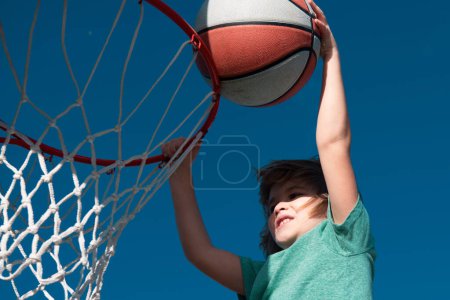 Foto de Chico divertido emocionado jugando baloncesto. Retrato infantil de primer plano. Cara de niño graciosa. Pequeño jugador de baloncesto haciendo slam dunk - Imagen libre de derechos