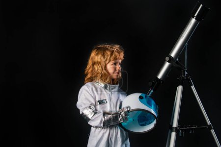 Foto de Un niño pequeño con telescopio y casco espacial sueña con convertirse en astronauta y volar al espacio. Cosmos niños en traje espacial y sueños casco. Éxito, creatividad y concepto de puesta en marcha - Imagen libre de derechos