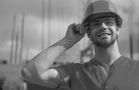 Téléchargez les photos : Portrait de constructeur masculin positif en casque dur travaillant sur le chantier de construction. Travailleur du constructeur dans le casque posant sur le chantier de construction - en image libre de droit