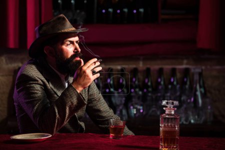 Téléchargez les photos : Un bel homme barbu dégustant du whisky au bar. Hipster avec barbe buvant un brandy au bar. Brutal mec boire de l'alcool - en image libre de droit