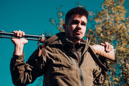 Téléchargez les photos : Saison de chasse fermée et ouverte. Un homme tenant un fusil. Braconnier avec fusil repérant des cerfs. Chasse illégale braconnier dans la forêt - en image libre de droit
