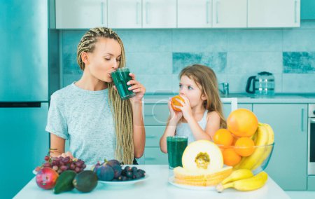 Photo for Happy family. Cute child eating breakfast at home. Eating and Healthy food. Healthy Lifestyle. Mother and child girl daughter drinking green smoothie in the kitchen with fruits and vegetables - Royalty Free Image