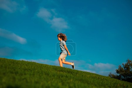 Photo for Happy child boy runs around the green field on blue sky, emotional walk on nature and happiness. Cute little boy having fun outdoors - Royalty Free Image