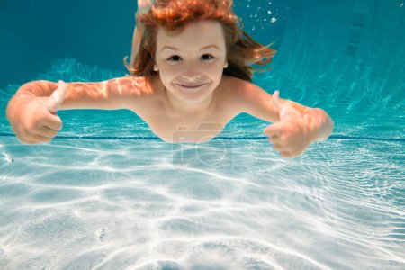 Foto de Niño en el agua nadando bajo el agua y sonriendo. Niño nadar bajo el agua en la piscina. Cara divertida de los niños - Imagen libre de derechos