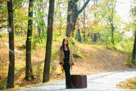 Foto de Otoño, moda, concepto de personas. Longitud completa de la mujer con maleta retro marrón caminando. Hojas que caen - Imagen libre de derechos