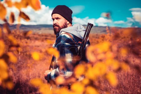 Photo for Autumn hunting season. Hunter with shotgun gun on hunt. Autunm hunting. Poacher with Rifle Spotting Some Deers. Close up Portrait of hamdsome Hunter - Royalty Free Image