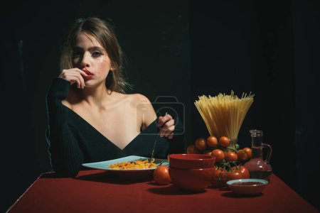 Photo for Gorgeous young brunette woman having Italian food. Seductive cheeky girl with plate of pasta eats pasta with ketchup - Royalty Free Image