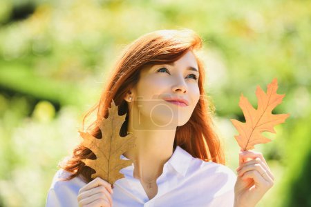 Photo for Beauty girl outdoors enjoying nature. Beautiful autumn female model holds yellow leaf near the face. Leafs falling and people concept - Royalty Free Image