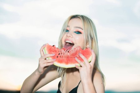 Téléchargez les photos : Gros portrait de jeune femme blonde sensuelle mangeant de la pastèque. Tropical vacances voyage sexy fille concept - en image libre de droit