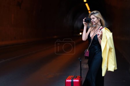 Foto de Sueños de viajar. Mujer turista en vestido de moda con maleta caminando por la calle. Chica estudiante viajero retrato al aire libre. Turista mujer teniendo viaje de vacaciones - Imagen libre de derechos