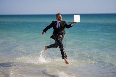 Photo for Fast business. Freelancer run outdoor. Businessman in suit with laptop running in sea water. Travel and tourism in sea. Fun employee with laptop running in sea. Business man run on summer vacation - Royalty Free Image
