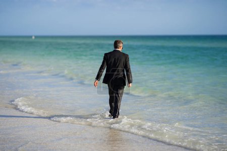 Photo for Rear view of back business man in suit in sea water at beach. Travel tourism and business concept. Crazy male office employee with laptop walk in sea. Crazy business man on summer vacation - Royalty Free Image