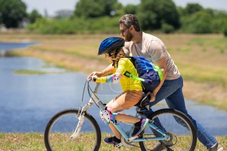Photo for Happy Fathers day. Father and son in bike helmet for learning to ride bicycle at park. Father helping son cycling. Father and son on the bicycle on summer day. Kid son trying to ride bike with father - Royalty Free Image