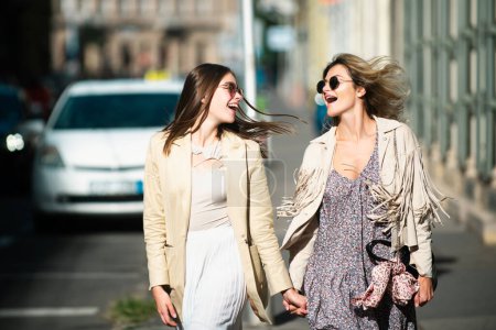 Foto de Dos jóvenes lanzadoras con gafas de sol caminando por la ciudad. Vacaciones divertidas, viajes románticos - Imagen libre de derechos