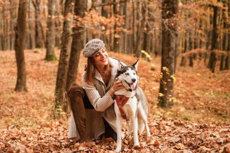 Foto de Chica de buen aspecto elegante está jugando con su perro husky en el bosque de otoño. El otoño es la mejor época del año para pasear con tu mascota. Naturaleza otoñal y paseo con concepto de mascota - Imagen libre de derechos