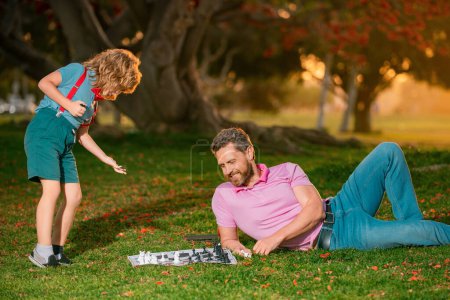 Foto de Padre e hijo jugando al ajedrez tendidos en el césped del parque. Día del Padre - Imagen libre de derechos