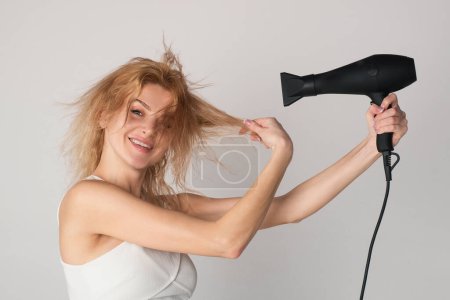 Foto de Hermosa mujer caucásica posando con el pelo mojado. Tratamiento del cabello de las mujeres. Chica con el pelo rubio usando secador de pelo. Peinado, concepto de peluquería - Imagen libre de derechos