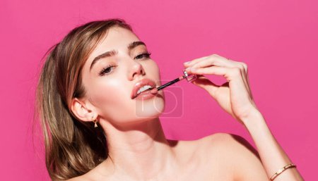 Foto de Young woman applies pink lipstick on sexy lips. Beautiful woman face with perfect makeup. Beauty girl with perfect skin - Imagen libre de derechos